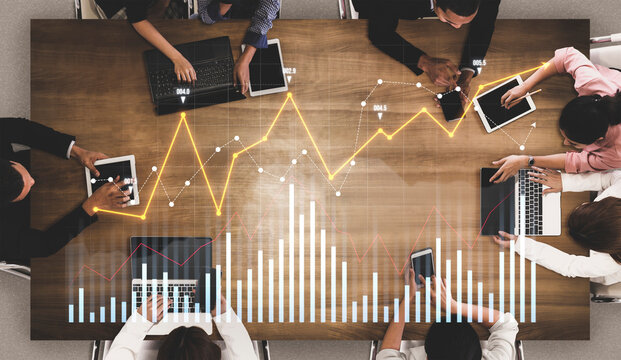 A group of professionals engage in a collaborative meeting at a conference table, using laptops and tablets to analyze data trends and visualize information in a modern office setting. Scalp