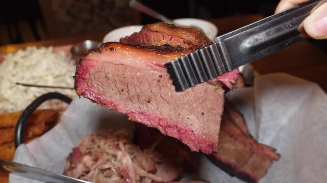 A high-quality close-up shot of a thick, juicy slice of tender, slow-cooked Texas-style beef brisket being held with metal tongs. The meat features a rich, dark peppery bark and a prominent reddish sm
