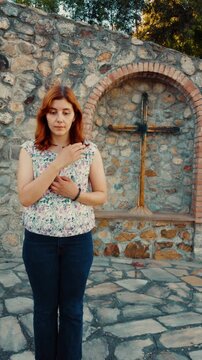 Woman makes the sign of the Christian cross with her hands near calvari sacred