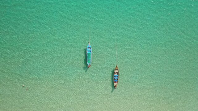 Phuket island, traditional longtail boats anchor in the crystal clear, shallow turquoise waters of the Andaman Sea, inviting travelers to explore the beautiful beach of Thailand. Aerial top down view