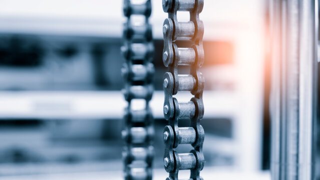 Metal chain hangs vertically in crisp focus. Background blurred with soft light streaks. Industrial setting suggests strength or function. tech industrial technology backgrounddesign