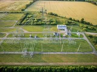 Electrical substation and high-voltage power lines situated among agricultural fields during sunset. Power grid infrastructure. © snapshotfreddy