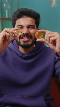 Indian man freelancer holding two gold coins successful developer programmer. Hindu boy stock trader earning bitcoins after online monitoring trading operations. Increasing wealth financial prosperity
