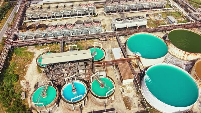 Aerial view of an industrial site featuring multiple large circular water tanks connected by pipes. Various shades of blue and green water fill the tanks.