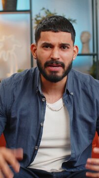 Hey you. Young upset bearded Indian man sitting on sofa looking with rage aggression, scolding protest, fighting to camera, displeasure, quarrel. Hispanic guy accusing for mistake at home apartment.
