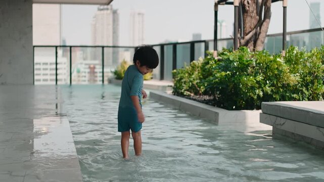 Happy young boy wading a shallow rooftop pool on a summer day