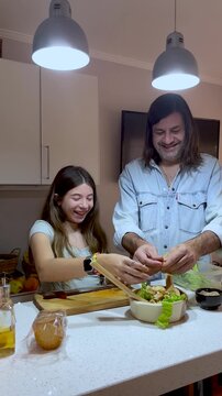 Vertical shot of a father and his teenage daughter working together in the kitchen and sharing smiles, demonstrating love,