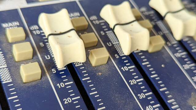 Macro shot of white fader sliders on an analog audio mixing console board with decibel level markings.