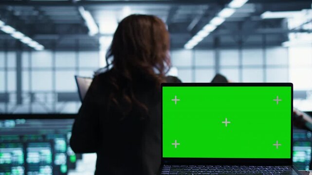 Mockup laptop with a replaceable screen is used beside software developers in a server farm, supporting chroma key editing, diagnostics and infrastructure review.
