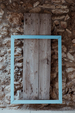 Weathered wooden planks framed in light blue against a stone wall create a rustic composition of texture and contrast, highlighting Mediterranean craftsmanship and timeless architectural simplicity.