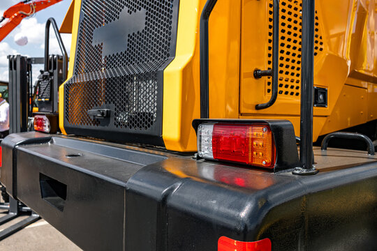 Industrial forklift rear bumper with tail light assembly. Modern heavy material handling machinery yellow chassis section with radiator grill grid mesh and warehouse logistics vehicle details.