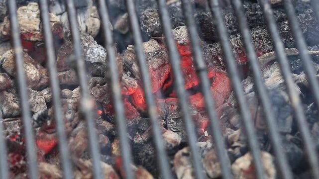 Glowing hot charcoal in barbecue grill pit with open flames close up background texture for bbq cooking and outdoor fire concept