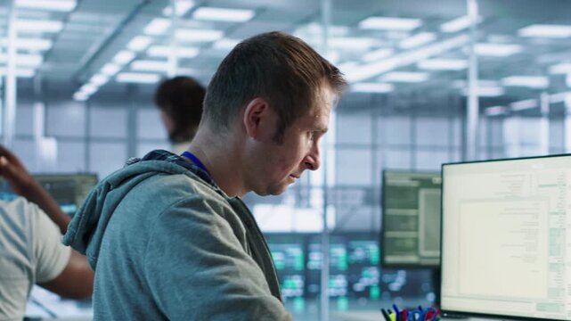 Smiling engineer inspecting server rows in data center while capturing firewall review, server bottlenecks and technical problem solving.