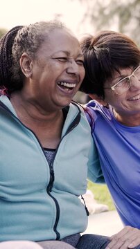 Happy multiracial senior women having fun at public park - Elderly people hugging each other