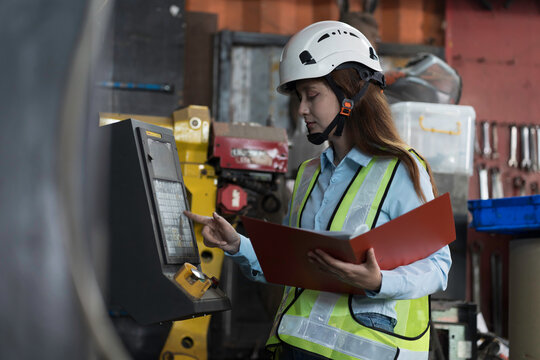 Woman worker working with clipboard for checking or inspecting in industry factory area, wearing safety helmet, uniform checking and working in the factory