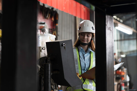 Woman worker working with clipboard for checking or inspecting in industry factory area, wearing safety helmet, uniform checking and working in the factory