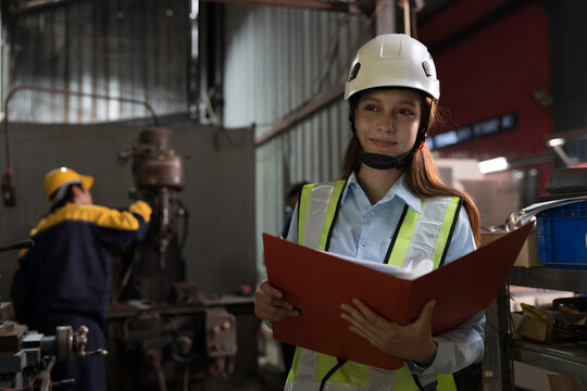 Woman worker working with clipboard for checking or inspecting in industry factory area, wearing safety helmet, uniform checking and working in the factory