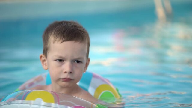 Young boy floating peacefully with a big smile in a colorful donut ring at the pool. Vibrant summer scene showcasing innocent joy, water fun and relaxing family holiday vibes.