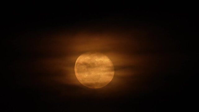 Luna naranja resplandeciendo entre nubes oscuras en el cielo nocturno.
