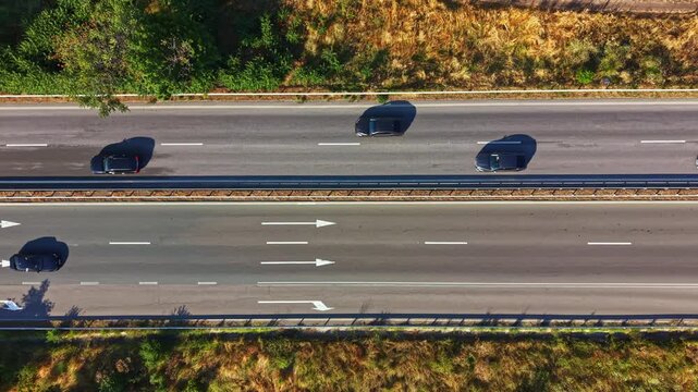 Two vehicles are moving along a straight highway that has clear lanes. The road is flanked by green trees and brown grass. It is daytime and the weather is clear.