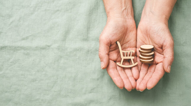 Hands holding a wooden rocking chair and a stack of coins representing retirement funds, pension security, and financial independence for seniors.