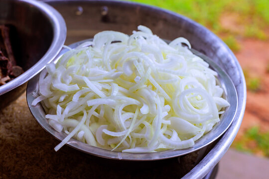 Fresh onions are cut into thin slices placed in metal bowl at food stall in busy area