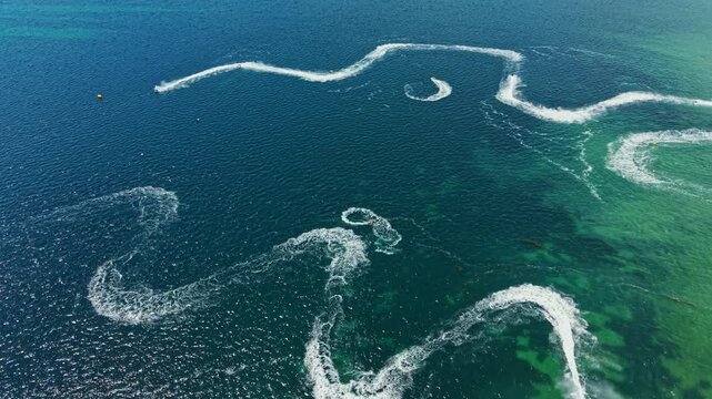 Riders compete on jet skis, creating waves and patterns on the surface of the water. This event occurs in a coastal setting with no visible land in the background.