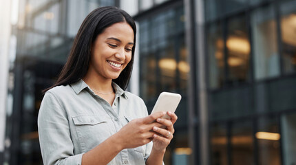 Fototapeta premium Young Professional Woman Smiling While Using Smartphone Outdoors in Front of Modern Glass Office Building