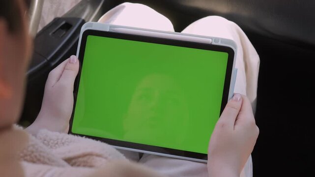 Person holds tablet with green screen. Hands steady, focused on device. Sitting inside car, relaxed posture. Green screen allows easy content replacement. Ideal for marketing, tutorials, or app demos