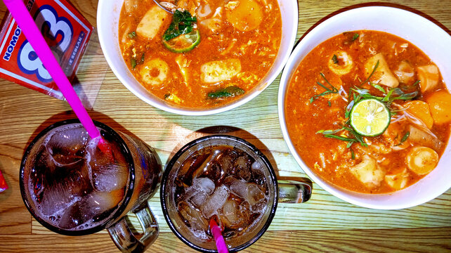 Top view of Indonesian spicy seblak soup bowls and iced tea drinks on wooden table