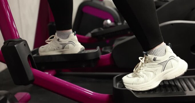 Overweight woman exercising with elliptical trainer in gym, closeup