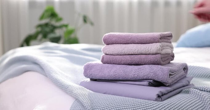 Home textile. Woman putting stack of terry towels on bed indoors, closeup