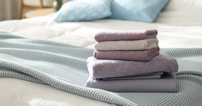 Home textile. Stack of terry towels and linens on bed indoors, closeup. Camera moving in