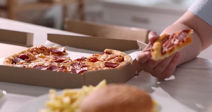 Overweight woman eating pizza and drinking cola at light table in kitchen. Camera moving forward