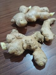 Fototapeta premium Whole fresh unpeeled ginger roots with rough skin laid on dark wooden table. Food ingredient concept 