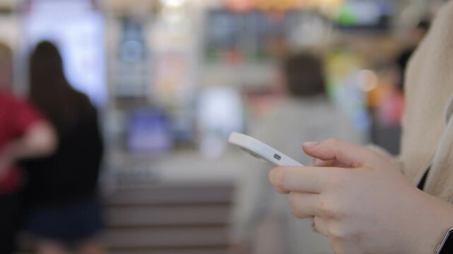 Hand holds phone in busy public space. Blurred background suggests movement and focus. Person seems calm, absorbed in device. Ideal for scenes of modern connectivity. Suitable for ads, tech content