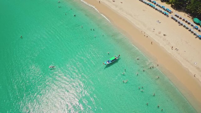 Karon beach in Phuket, aerial drone view on turquoise waters and white sand, people swimming, sunbathing under umbrellas, and a traditional longtail boat. Travel to Thailand. Summer holiday vacation