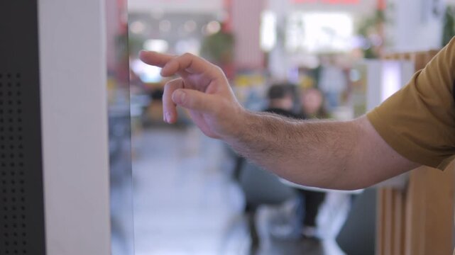 Hand taps glass screen in modern cafe. Blurred background shows cafe seating. Action suggests user interacts with digital interface. Ideal for tech, hospitality, or urban lifestyle themes