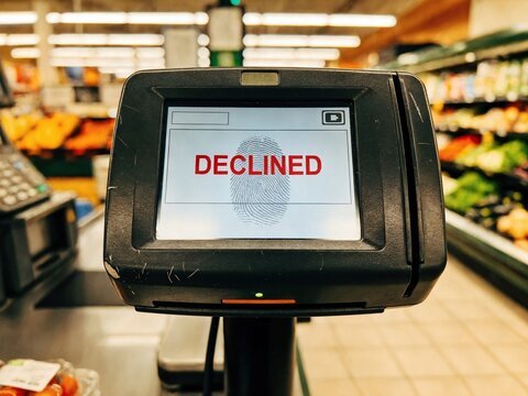 Close-up of a payment terminal in a grocery store checkout area, showing a declined transaction with a fingerprint scanner