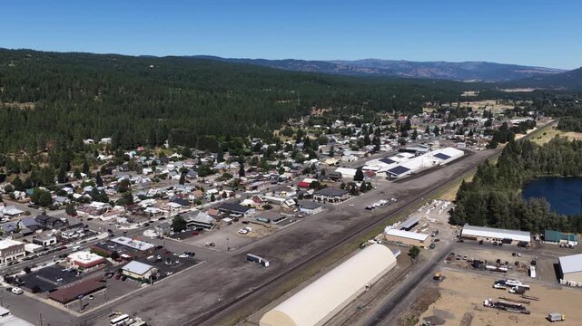 Aerial of small town and railroad tracks in Cle Elum Washington with dense coniferous forest surrounding the commercial and industrial area