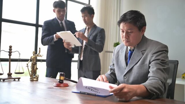 Lawyer reading contract with colleagues discussing in background
