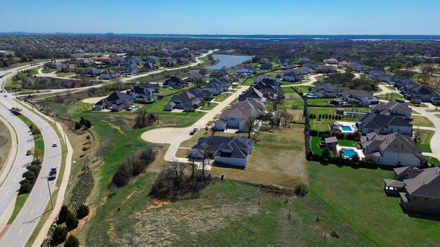 Lake Lewisville shorelines extend near Dallas suburb Bridlewood neighborhood. High angle perspective frames luxury executive residences, swimming pools, open land. Flower Mound, TX