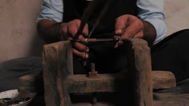 Close-up cinematic footage of an artisan using a traditional bow drill and wooden vise for manual craftsmanship in a dimly lit workshop.