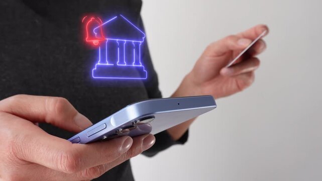 Businesswoman holding a bank card while holding a smartphone with a virtual icon of a bank with notification bell