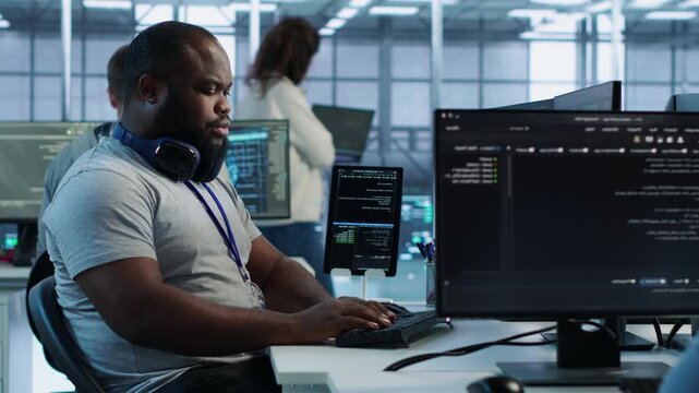 Cheerful IT specialist monitoring high tech supercomputers using tablet while showing secure storage, threat prevention and cybersecurity monitoring.
