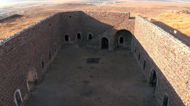 Aerial pull-back drone footage revealing a historic stone fortress and its inner courtyard situated on an arid, hilly landscape.