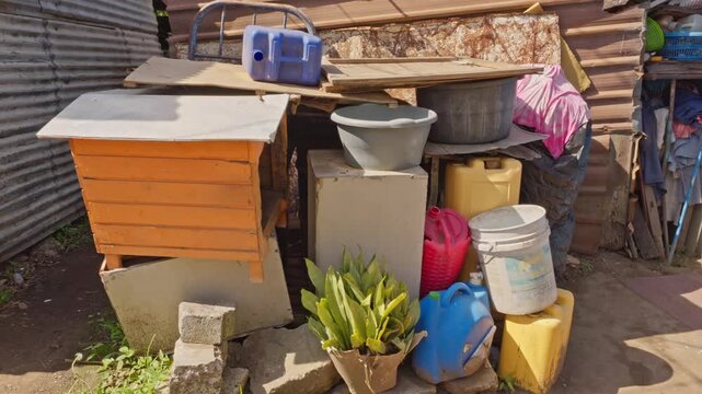 Cluster of various plastic containers, colored jugs, buckets, and a small wooden kennel-like structure stacked in the outdoor yard.