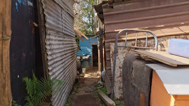 Perspective through a narrow corridor between corrugated sheet metal walls leading toward the back of the community plot.