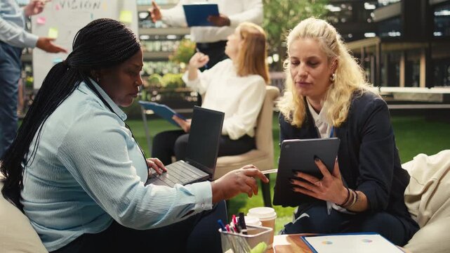 Diverse business team discusses planning ideas near vision board during outdoor session, sharing strategy ideas with tablet and notebook, informal collaboration in business park, for planning notes.