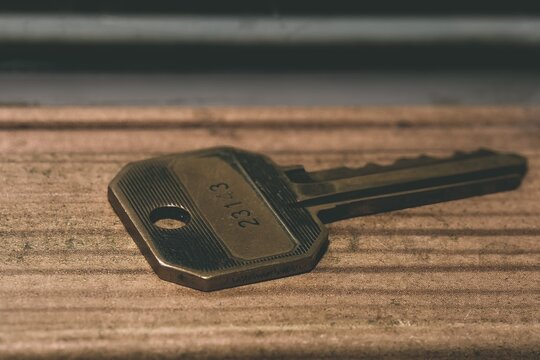Macro close up shot of a vintage brass door key resting on a rustic wooden surface with serial number code stamped on it